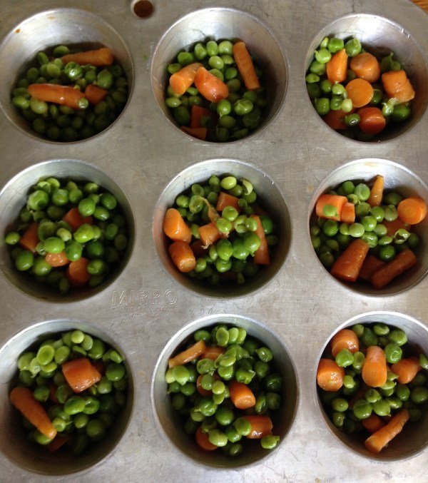 muffin tin filled with peas and carrots